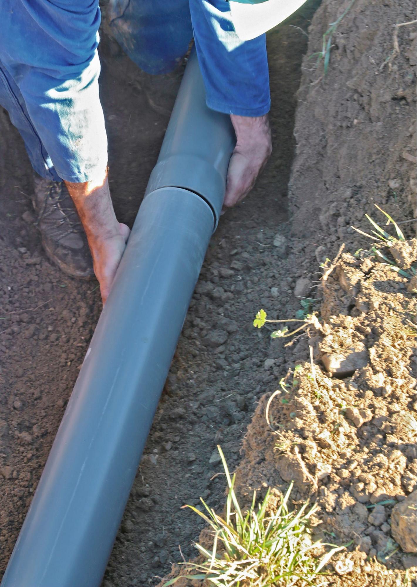 Worker laying perforated pipe in a gravel trench during a french drain installation