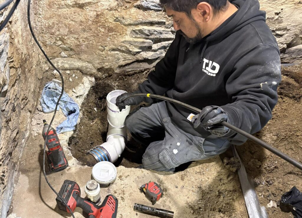 TID Trenchless technician running a drain cable through a basement sewer cleanout in Dedham, MA.