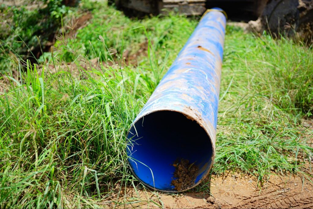 Length of new pipe resting on a grassy yard near a work site